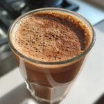 Close-up of a frothy Cacao Almond Energy Shake in a glass, ready to drink.