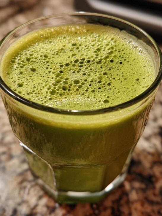A close-up of a vibrant green Cranberry Beet Endurance Drink in a glass, topped with frothy bubbles.