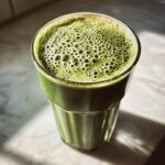 A close-up of a vibrant green Cranberry Beet Endurance Drink with frothy bubbles on top.