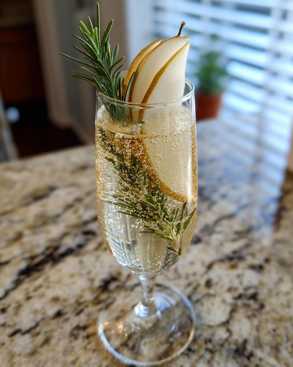 A refreshing Ginger Pear Champagne Cocktail garnished with pear slices and a sprig of rosemary.