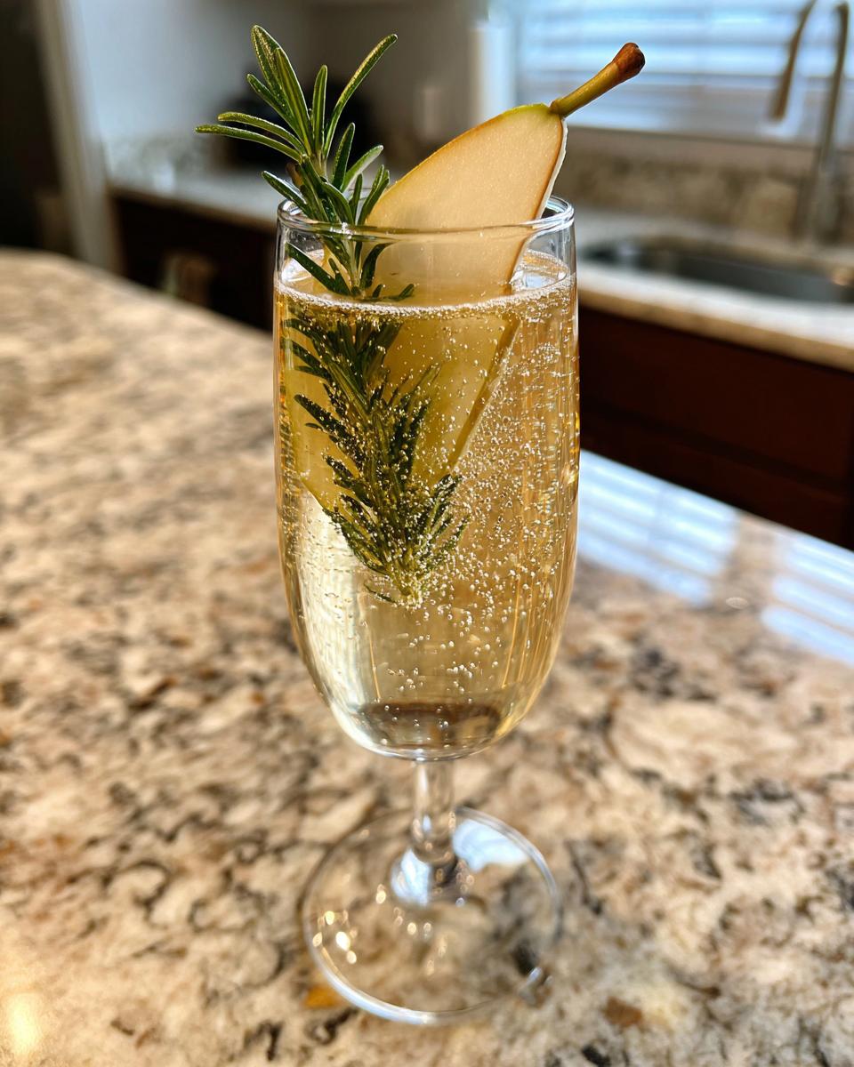A festive Ginger Pear Champagne Cocktail garnished with a pear slice and fresh rosemary sprig.