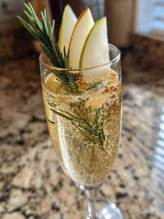 A festive Ginger Pear Champagne Cocktail garnished with pear slices and rosemary sprig.