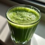 A glass filled with vibrant green Guarana Coconut Energy Tonic, topped with foam, in natural light.