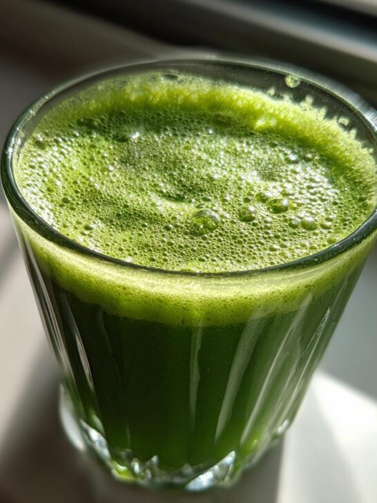 A glass filled with vibrant green Guarana Coconut Energy Tonic, topped with foam, in natural light.