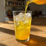 Pouring a bright yellow Honey Lemon Turmeric Spritzer into a glass filled with ice.