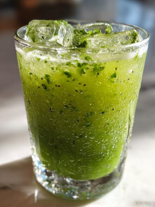 A tall glass filled with a vibrant green Kiwi Spinach Detox Mocktail, packed with ice and garnished with fresh mint.