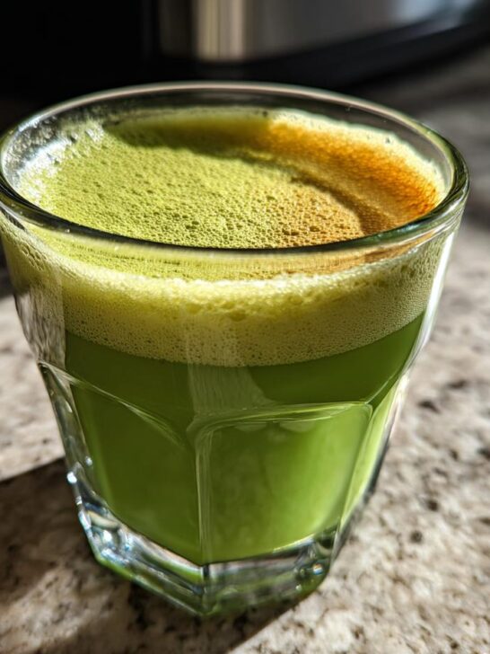 A frothy Matcha Green Energy Latte in a clear glass, with sunlight hitting the surface.