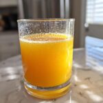 A glass of vibrant orange Pineapple Spirulina Energizer drink with bubbles, ready to be enjoyed.