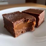 Two squares of rich Brown Sugar Fudge with a visible caramel center and chocolate topping, one with a bite taken out.