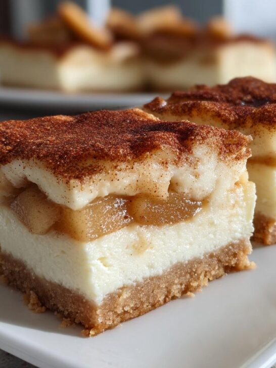 Two perfect squares of Apple Cheesecake Bars showing a graham cracker crust, creamy filling, and spiced apple topping dusted with cinnamon.