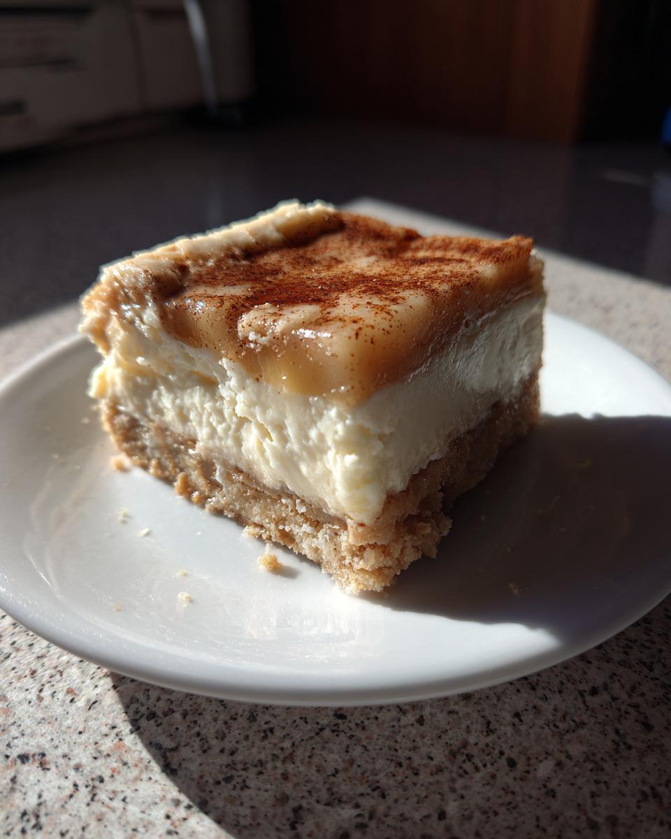 A close-up of one square portion of Apple Cheesecake Bars with a creamy filling and cinnamon topping.