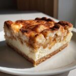 A close-up of a thick slice of Apple Cheesecake Bars showing graham cracker crust, creamy filling, and spiced apple topping.