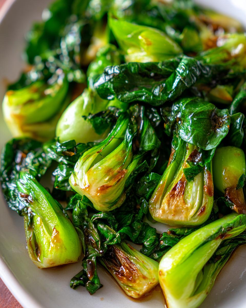 Close-up of a white platter filled with glistening, stir-fried Baby Bok Choy, showcasing its vibrant green leaves and tender stems.
