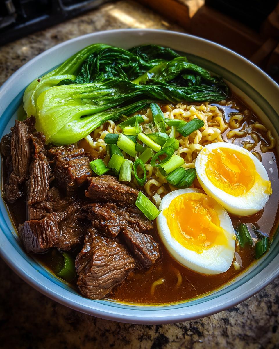 A close-up of a bowl of Beef Ramen Recipe, featuring tender beef slices, ramen noodles, bok choy, scallions, and a soft-boiled egg.