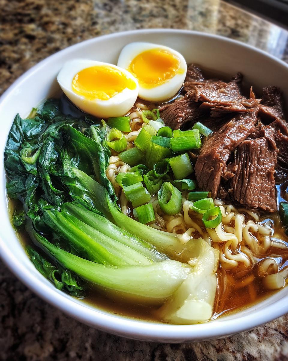 A close-up of a steaming bowl of Beef Ramen Recipe, featuring noodles, tender beef, bok choy, and a soft-boiled egg.