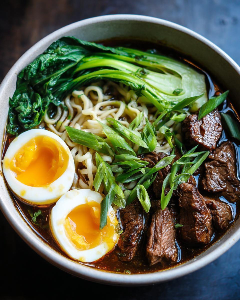 A close-up of a steaming bowl of Beef Ramen Recipe, featuring tender beef slices, ramen noodles, bok choy, and a perfectly soft-boiled egg.