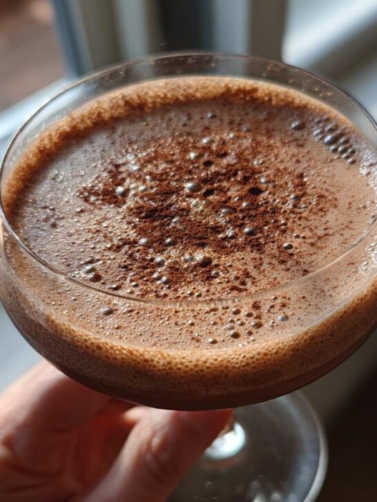 Close-up of a frothy chocolate cocktail in a coupe glass, dusted with cocoa powder.