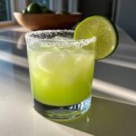 A vibrant green Margarita cocktail in a salt-rimmed glass, garnished with a lime wedge. Best Cointreau Cocktails.