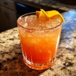 A vibrant orange cocktail made with best non alcoholic spirits, served over ice and garnished with orange slices.