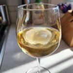 A close-up of a glass filled with golden nonalcoholic white wine, with small bubbles visible.