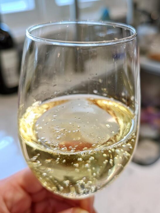 Close-up of a hand holding a glass filled with bubbly, golden nonalcoholic white wine.