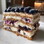 A close-up of a layered slice of Blueberry Cheesecake Icebox Cake topped with fresh blueberries.
