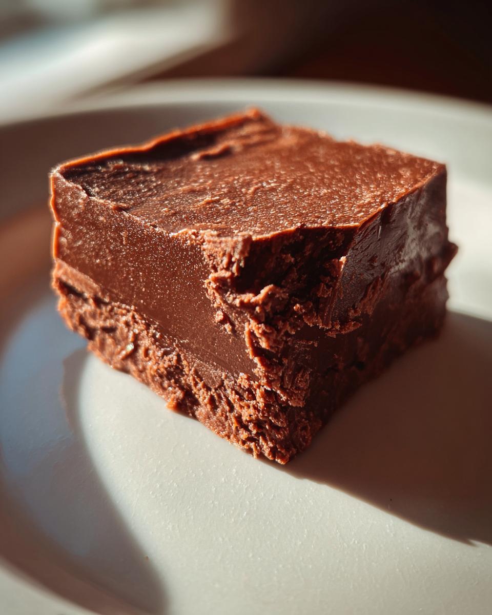 A close-up, sunlit square of rich, dark brown sugar fudge resting on a white ceramic plate.