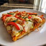 A delicious slice of Cajun Veggie Pumpkin Pizza topped with melted cheese, red peppers, zucchini, and onions.