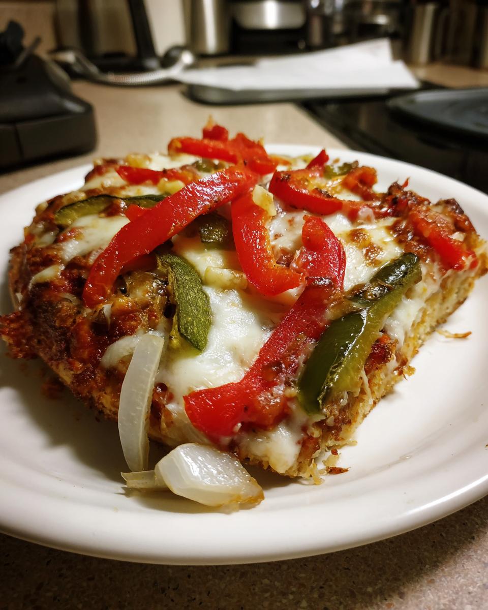 A delicious slice of Cajun Veggie Pumpkin Pizza topped with melted cheese, red and green bell peppers, and onions.