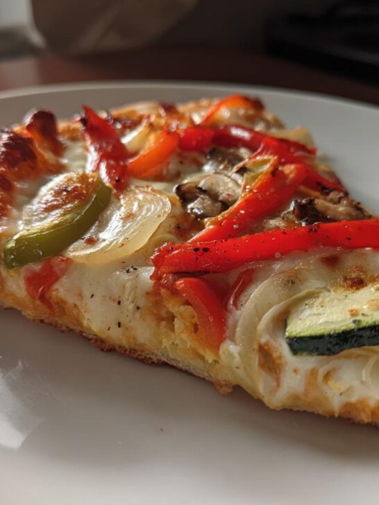 A slice of Cajun Veggie Pumpkin Pizza featuring melted cheese, red and green bell peppers, onions, and zucchini.