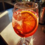 Close-up of a vibrant orange Campari Spritz cocktail in a wine glass, filled with ice and garnished with an orange slice.