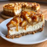 A decadent slice of Caramel Apple Cheesecake on a white plate, topped with thick caramel sauce and apple pieces.