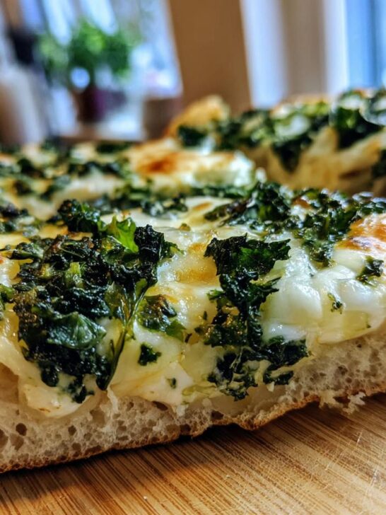 A close-up of a slice of The Best Cheesy Kale Garlic Bread, showcasing melted cheese and kale on a golden crust.