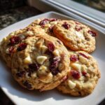 Four chewy Cranberry White Chocolate Cookies piled on a white square plate, featuring visible white chocolate chips and dried cranberries.