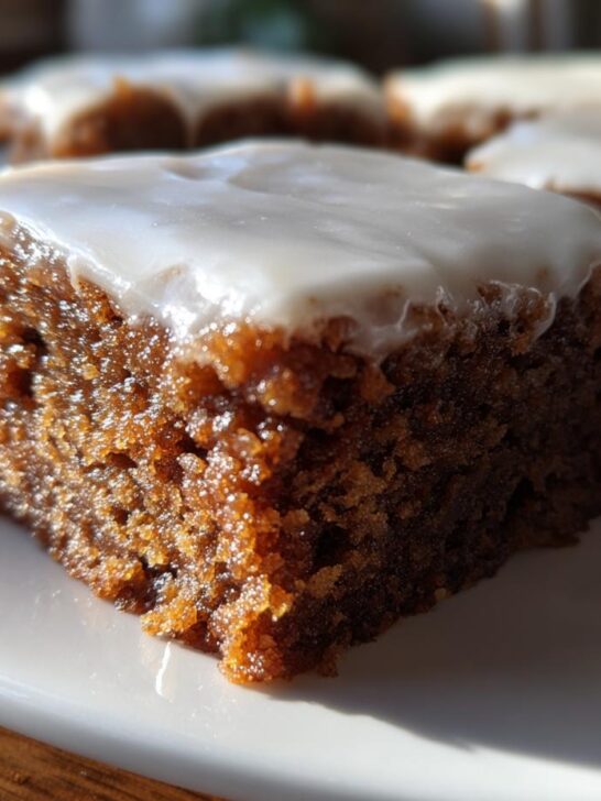 Close-up of a moist, dark brown Gingerbread Cookie Bars square topped with thick white icing.