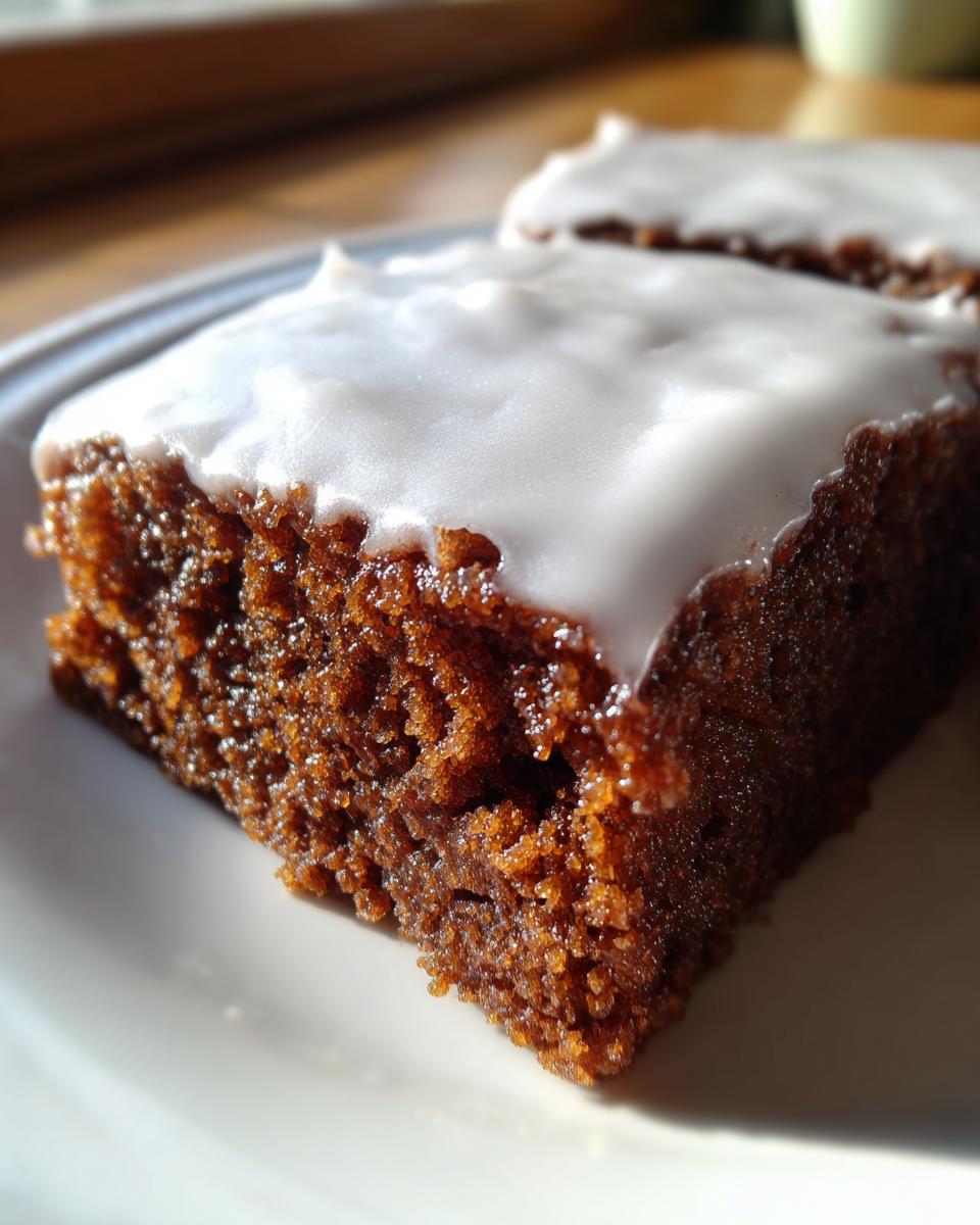Close-up of a moist, dark brown Gingerbread Cookie Bars slice topped with thick white icing.