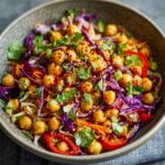 A close-up of a colorful chickpea salad in a bowl, featuring chickpeas, shredded red cabbage, carrots, bell peppers, and fresh cilantro.