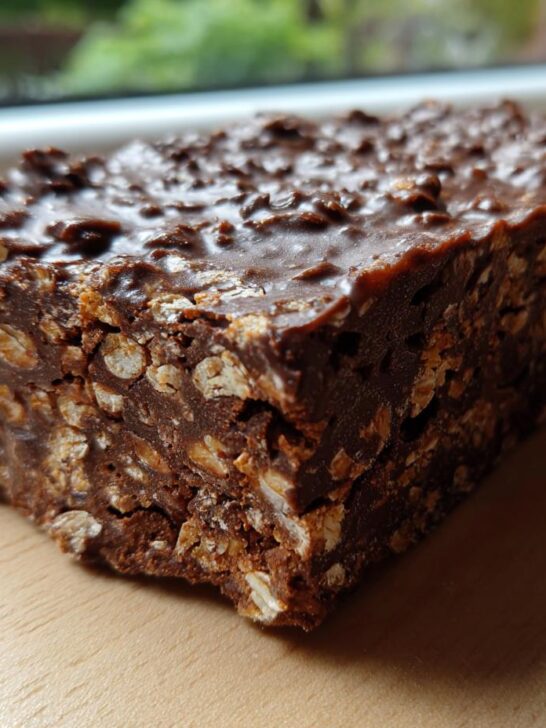 A close-up, rectangular slice of dense Chocolate Biscuit Cake showing oats/biscuits bound in dark chocolate.