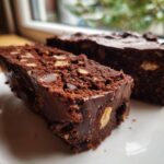 Two rich slices of dense Chocolate Biscuit Cake studded with visible nuts, served on a white plate.