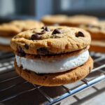 Close-up of a Chocolate Chip Sandwich Cookie filled with thick white cream, resting on a wire rack.