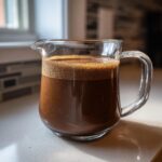 A glass pitcher filled with frothy chocolate oat milk, ready to be served.