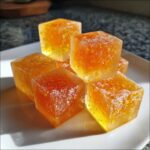 A pile of glistening Citrus Ginger Turmeric Ice Cubes on a white plate, showing their vibrant orange and yellow hues.