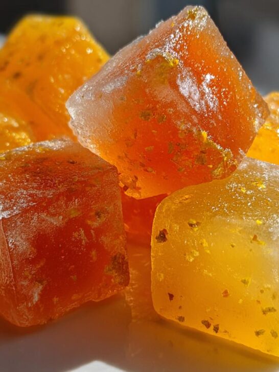 Close-up of bright orange and yellow Citrus Ginger Turmeric Ice Cubes with visible flecks of ginger and turmeric.