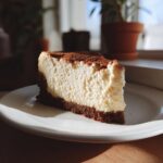 A perfect slice of Coffee Cheesecake with a thick, creamy filling and dark crust, dusted with cocoa powder.