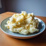 A generous serving of creamy mashed potatoes, drizzled with melted butter, presented on a blue plate.
