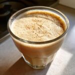 A close-up of a glass filled with creamy vanilla sesame milk, topped with a frothy layer.