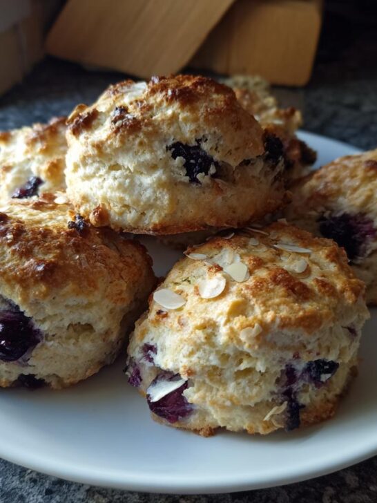 A plate of delicious Dairy Free Blueberry Almond Scones, topped with sliced almonds and bursting with blueberries.