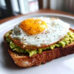 Close-up of delicious avocado toast with a perfectly fried egg and cracked pepper.