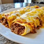 Close-up of two Delicious Easy Ground Beef Enchiladas covered in melted cheese and sauce on a white plate.