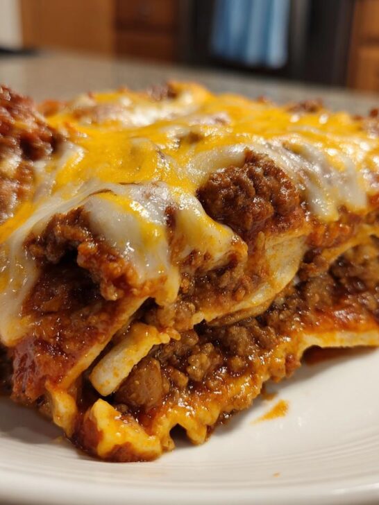 A close-up of a slice of Delicious Easy Ground Beef Enchiladas, showing layers of meat, sauce, and melted cheese.